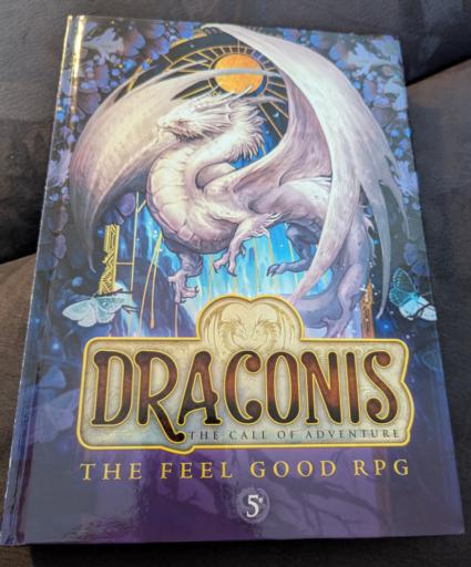 A picture of the draconis RPG book. On the front one sees a majestic white dragon in a non threatening way