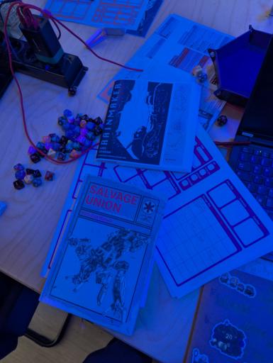 Tisch voller verschiedener Würfel und Beschreibungen von mechs und Karten aus dem Spiel salvage union