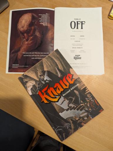 Das Abenteuerbuch aufgeschlagen, darauf liegt das kleine A5 knave Regelbuch