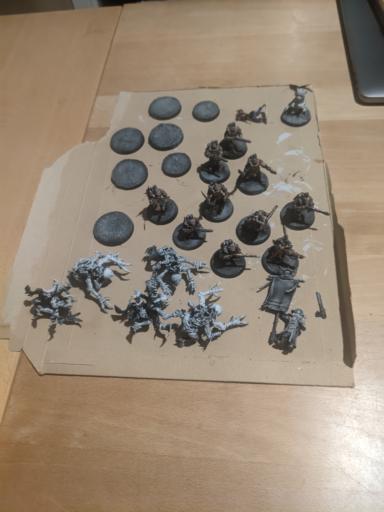 Picture of a dozen half painted miniatures sitting on a piece of cardboard. half of them are sci fi solar guards, the other half are gene stealer like monsters with four arms and claws.