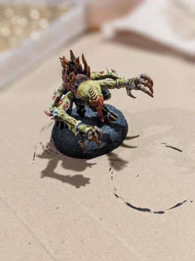 A painted monste with four arms and a alien like face and a long tongue.