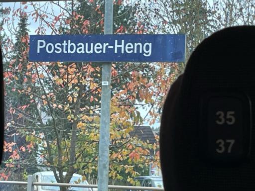 Foto aus dem Zugfenster auf das Bahnhofs-Schild „Postbauer-Heng“