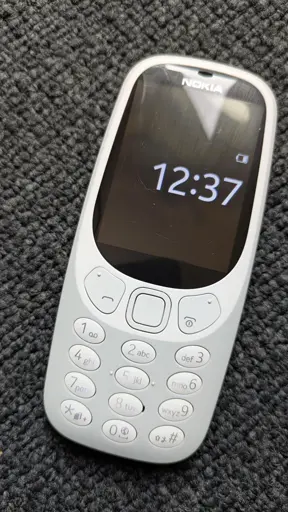 Es ist ein altmodisches NOKIA-Handy zu sehen. Auf dem Display die Uhrzeit 12:37.